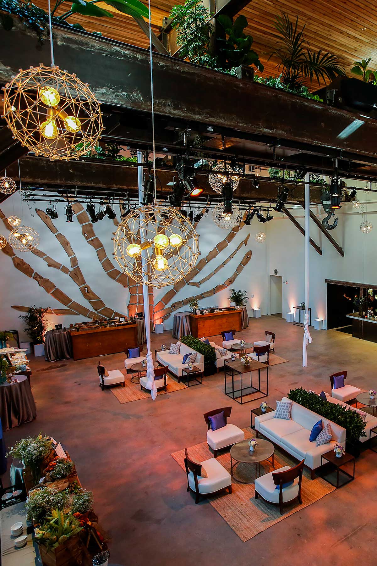 Spacious modern event space with hanging spherical pendant lights, lounge seating with white sofas and chairs, and decorative wooden wall art.