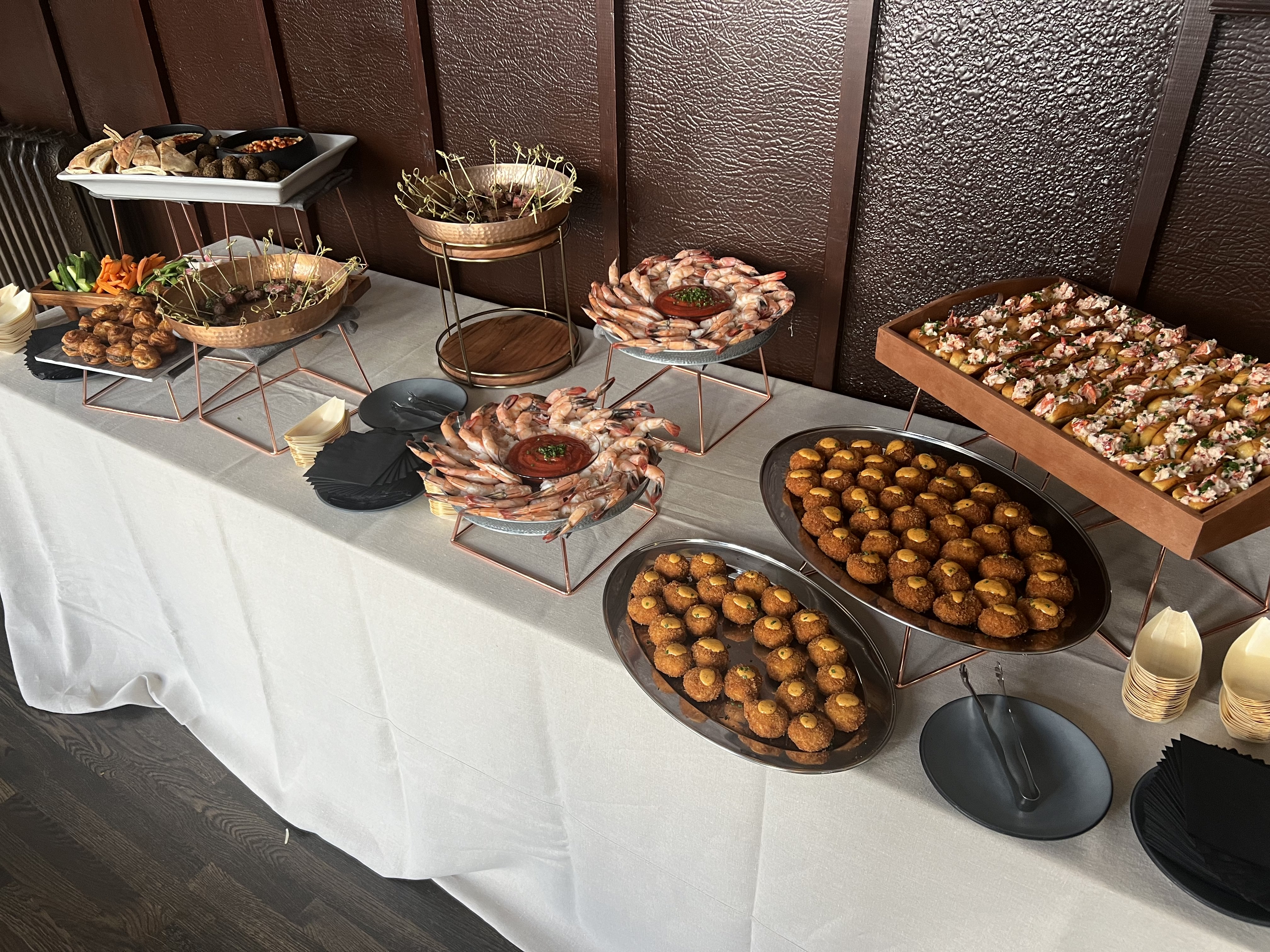 Buffet table with shrimp cocktail, assorted appetizers, vegetable sticks, and small plates on a white tablecloth.