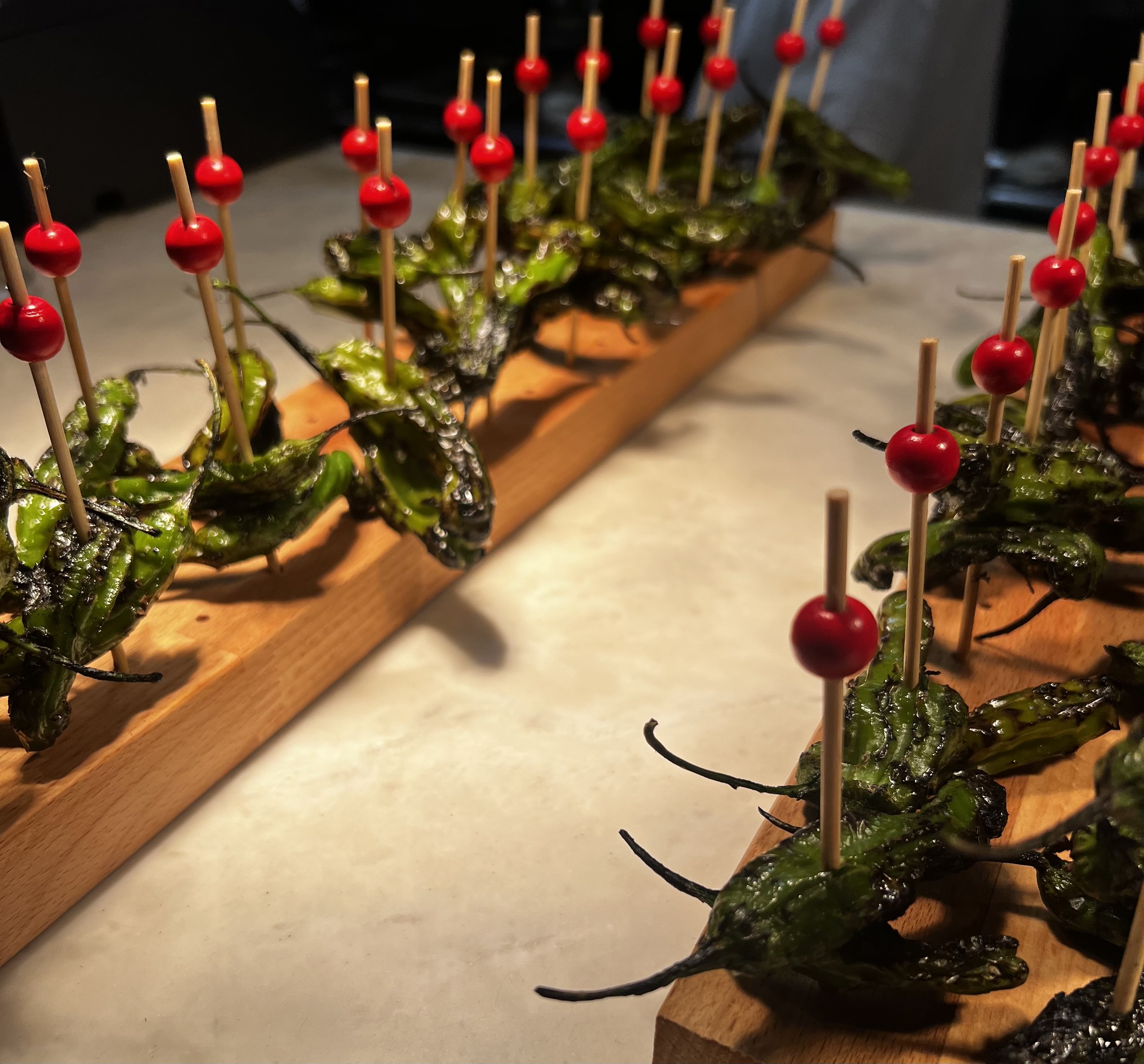 Skewers of grilled green peppers with red bead decorations, arranged on wooden boards.