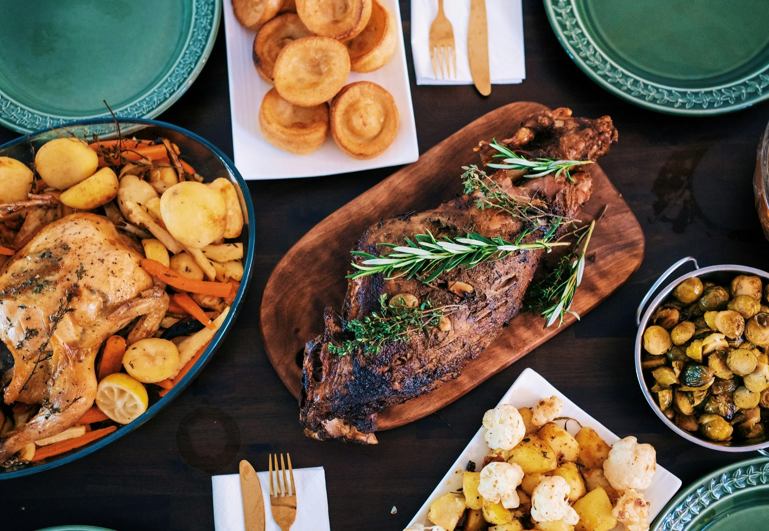 Dinner table with roasted whole chicken with vegetables, roast pork garnished with rosemary, roast potatoes with cauliflower, Brussels sprouts, and Yorkshire puddings.