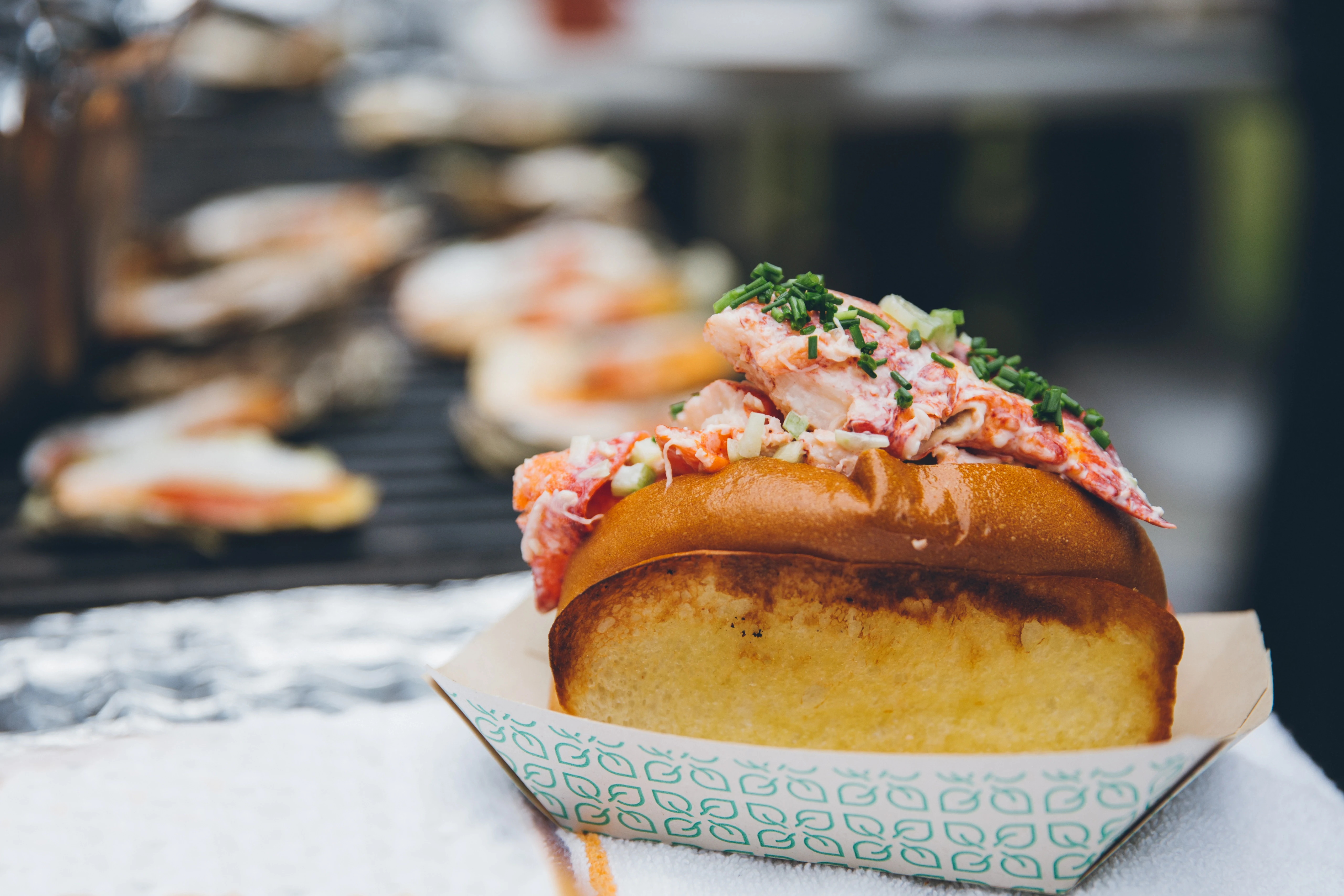 Lobster roll with fresh lobster meat and chives in toasted bun on a paper tray.